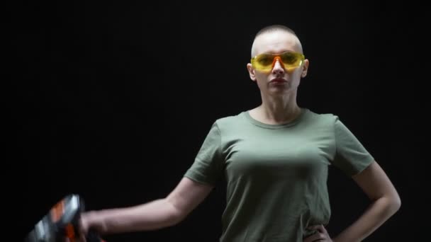 Beautiful bald woman in safety glasses with a drill in her hands on a black background — Stockvideo