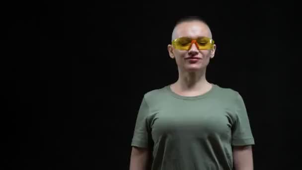 Beautiful bald woman in protective glasses with an adjustable wrench in her hands on a black background. humorous concept — Stock Video