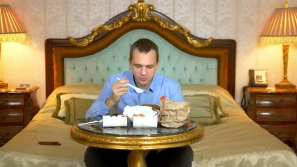 Primer plano. Hombre de negocios guapo está comiendo comida rápida sentado en la cama en un interior de lujo . — Vídeo de stock