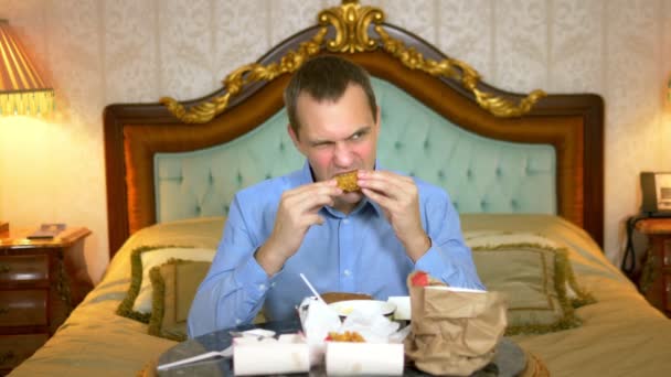 Close-up. Knappe zakenman eet fastfood zittend op het bed in een luxe interieur. — Stockvideo