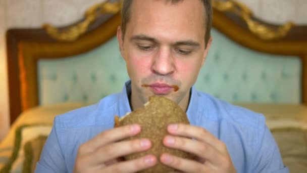 Primer plano. Hombre de negocios guapo está comiendo comida rápida sentado en la cama en un interior de lujo . — Vídeo de stock