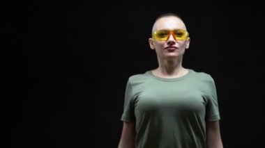 Güvenlik gözlüklü güzel kel kadın elinde matkapla siyah bir arka planda.