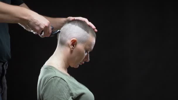 Konsep gadis militer. Tangan seorang pria penata rambut mencukur kepala wanita botak, gaya rambut tentara. Latar belakang hitam — Stok Video