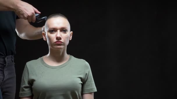 Concept fille militaire. mains d'un homme coiffeur raser une femme chauve tête, coiffure de l'armée. Fond noir — Video