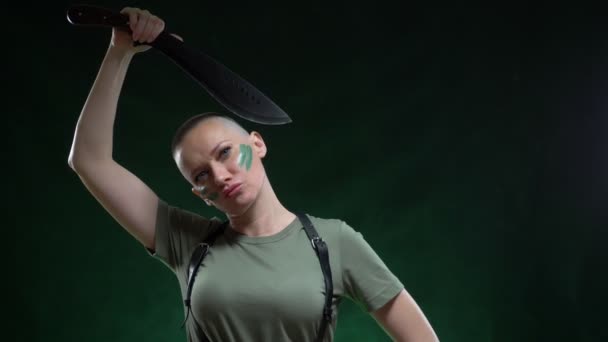 Angry bald girl with camouflage makeup shaving machete hair on a black background — Stockvideo