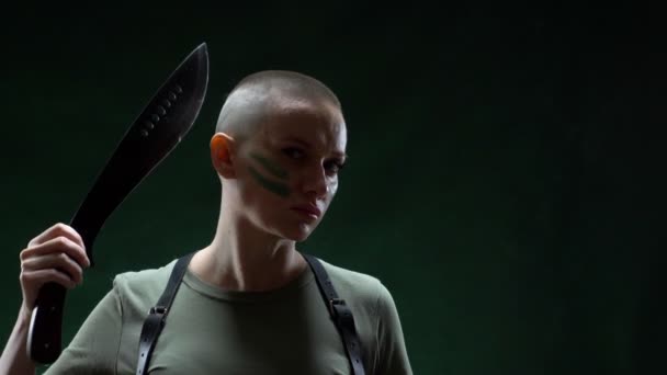 Angry bald girl with camouflage makeup shaving machete hair on a black background — Stockvideo