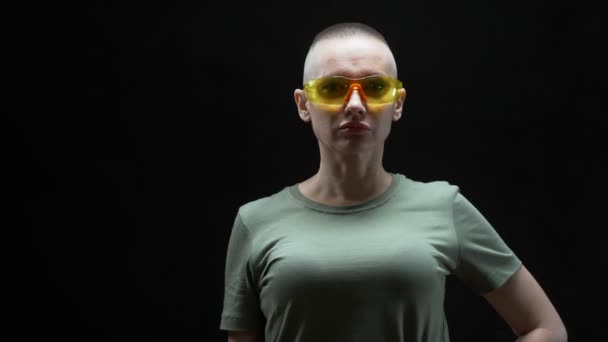 Schöne glatzköpfige Frau in Schutzbrille mit einem Bohrer in den Händen auf schwarzem Hintergrund — Stockvideo
