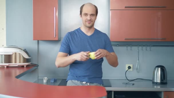 De kalende jongeman die thee drinkt in de keuken. kijkend naar de camera — Stockvideo