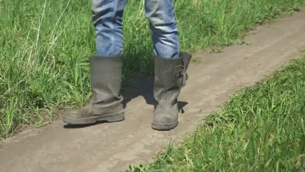 Voeten van dichtbij. de man in canvas laarzen komt langs de weg in het veld — Stockvideo