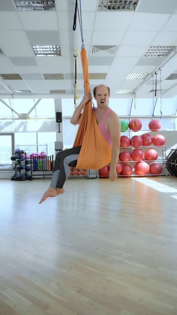 Verticaal. vrolijke, lachende kalende man in een hangmat voor luchtyoga lessen. — Stockvideo