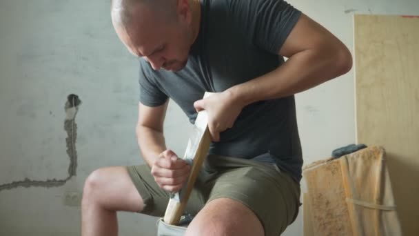 Careca homem aviões uma plaina barra de madeira sentado dentro de casa — Vídeo de Stock