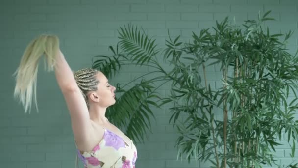 Женщина с афрокосичками и длинным хвостиком на фоне комнатных растений — стоковое видео