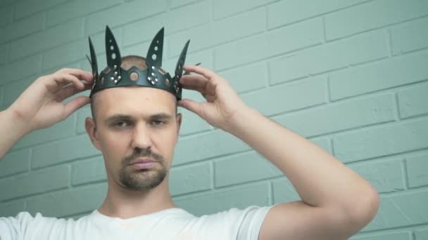 Handsome strange man in a white t-shirt puts on his head a leather black crown — Stock Video