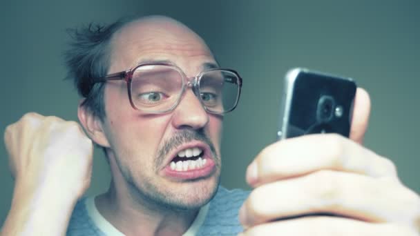 Een kale man met een bril gebruikt een smartphone. gebaar verrassingsoverwinning. Humor — Stockvideo