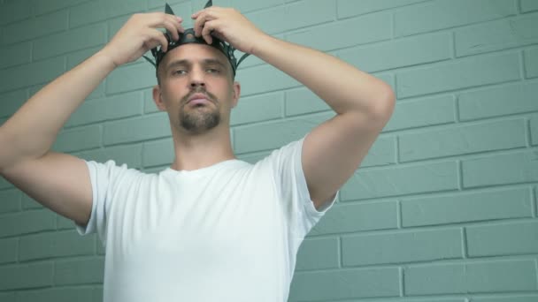 Stilig främmande man i en vit t-shirt sätter på huvudet en läder svart krona — Stockvideo