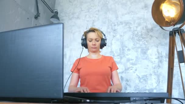 Woman produces electronic music in the studio with a laptop and midi keyboard — Stock Video