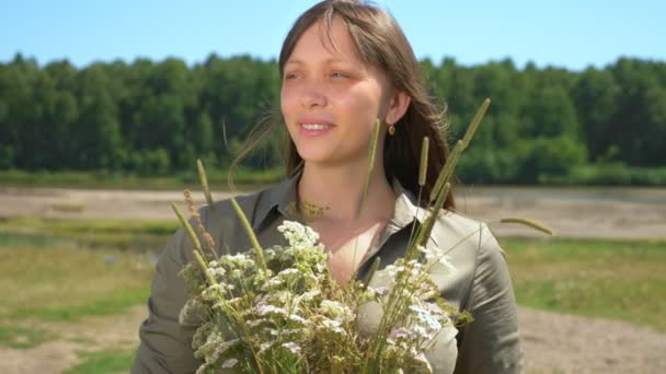Portrét krásné dívky s kyticí divokých květin u řeky — Stock video