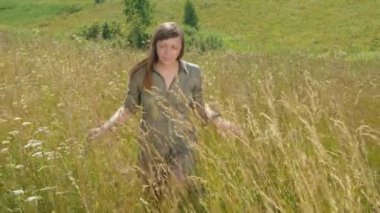Güzel genç bir kadın uzun otların arasında yürüyor