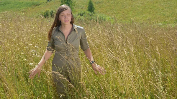Schöne junge Frau geht über ein Feld im hohen Gras — Stockfoto