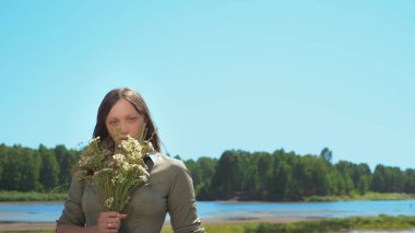 Güneşli bir yaz gününde elinde bir buket kır çiçeğiyle güzel bir kızın portresi.