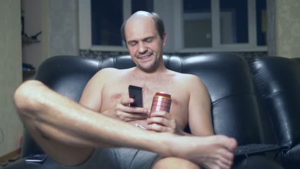 Pria botak kesepian di rumah di kursi dengan bir dan remote control. — Stok Video