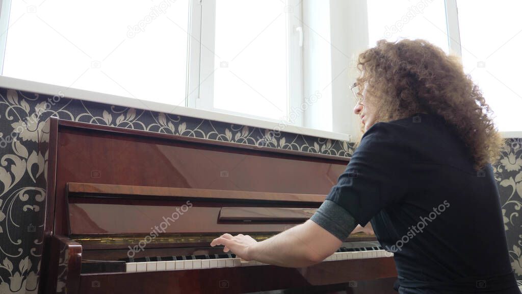beautiful girl in glasses with curly hair plays the piano. side view