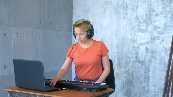 Nő termel elektronikus zene a stúdióban egy laptop és midi billentyűzet — Stock Fotó
