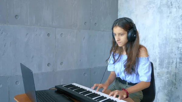 在网上带耳机的女孩学习在笔记本电脑上弹钢琴 — 图库照片