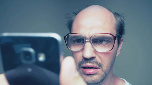 Balding man with glasses hardly uses a smartphone. Humor — Stock Photo, Image