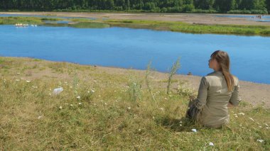 Arka manzara, uzun saçlı sarışın kız nehir kıyısında oturuyor.