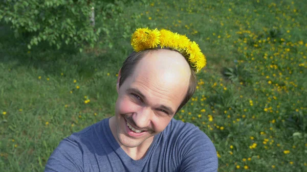 Um homem careca com uma coroa de dentes-de-leão na cabeça. a olhar para a câmara — Fotografia de Stock