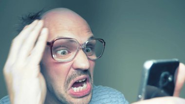 Gözlüklü kel bir adam akıllı telefon kullanır. jest sürpriz zafer. Mizah