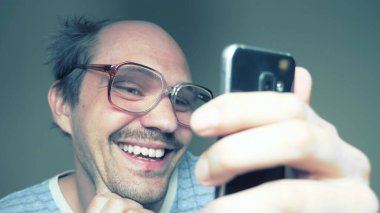 Gözlüklü komik kel adam akıllı telefon kullanıyor ve gülümsüyor.
