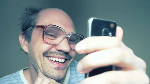 funny balding man in glasses uses a smartphone and smiles