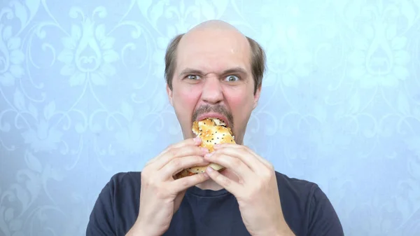 portrait hungry mustachioed balding man bites a hamburger