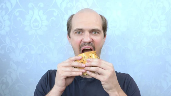 Retrato fome bigode careca homem morde um hambúrguer — Fotografia de Stock