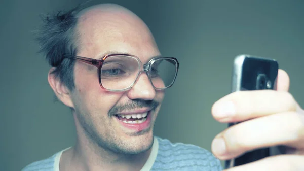 Funny balding man in glasses uses a smartphone and smiles — Stock Photo, Image