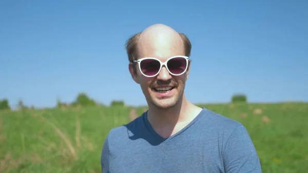 Портрет. веселый лысый парень в солнечных очках в поле в ясный солнечный день — стоковое фото