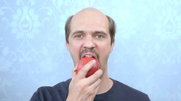 Retrato de un feliz hombre calvo bigotudo muerde una manzana roja — Foto de Stock