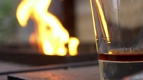 Boisson alcoolisée brune au fond du verre sur fond de feu — Video