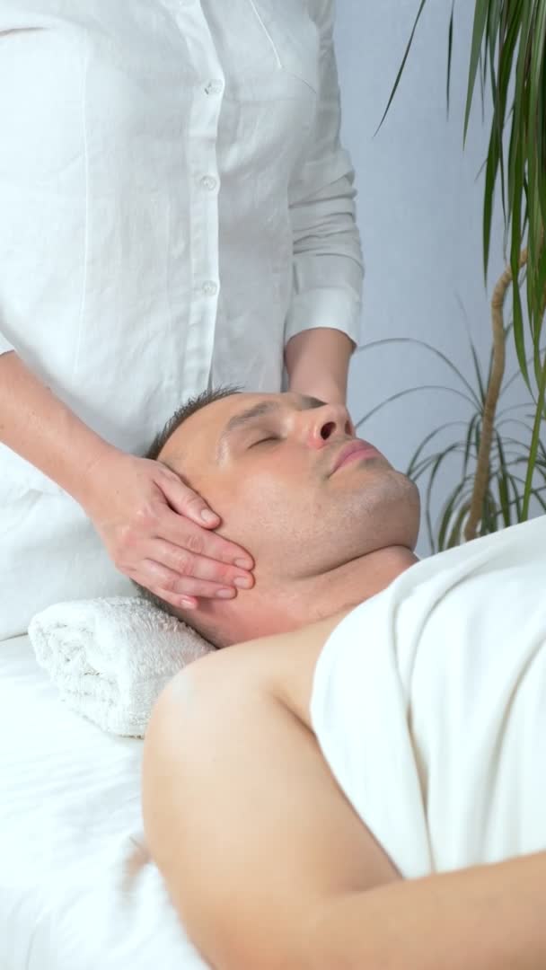 Pionowo, masażystka robi kosmetyczny masaż twarzy mężczyźnie w salonie spa — Wideo stockowe