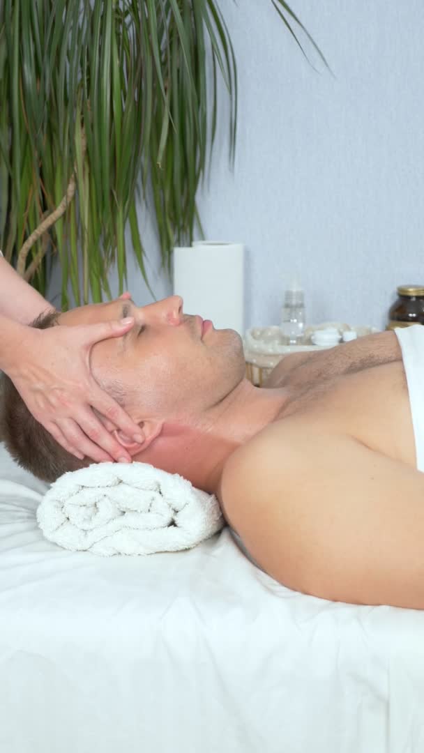Verticalmente, massagista faz uma massagem facial cosmética para um homem em um salão de spa — Vídeo de Stock
