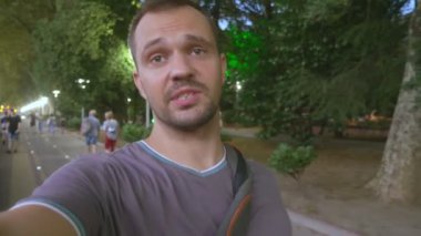 Beyaz erkek blogcu nehir kenarındaki kameraya bakarak konuşuyor.