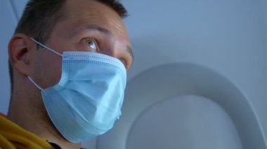 Yakın plan. Pencere kenarındaki uçakta maskeli bir adamın portresi.