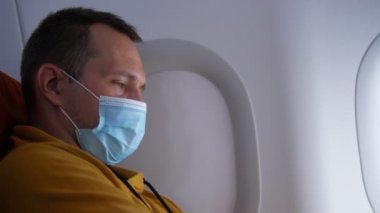 Yakın plan. Pencere kenarındaki uçakta maskeli bir adamın portresi.