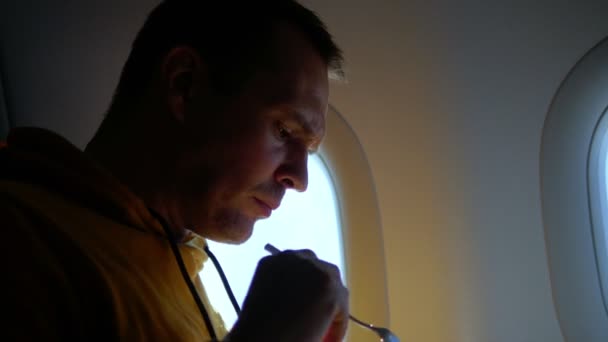 Человек ест еду авиакомпании в самолете на фоне окна — стоковое видео