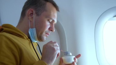 Maskeli bir adam uçakta otururken plastik bir bardaktan su içer.