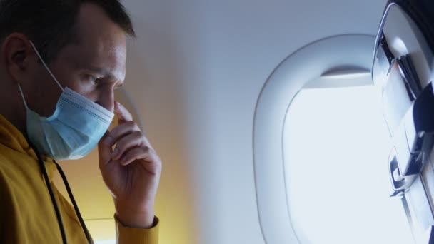 Ein maskierter Mann trinkt im Flugzeug ein Getränk aus einem Plastikglas — Stockvideo