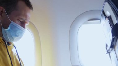 Maskeli bir adam uçakta otururken plastik bir bardaktan su içer.