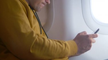 Elleri yakın çekim. Bir adam uçakta otururken akıllı telefon kullanır.